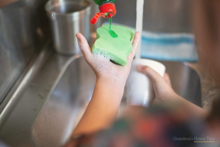 Pouring grease-cutting dish soap onto a sponge at the kitchen sink