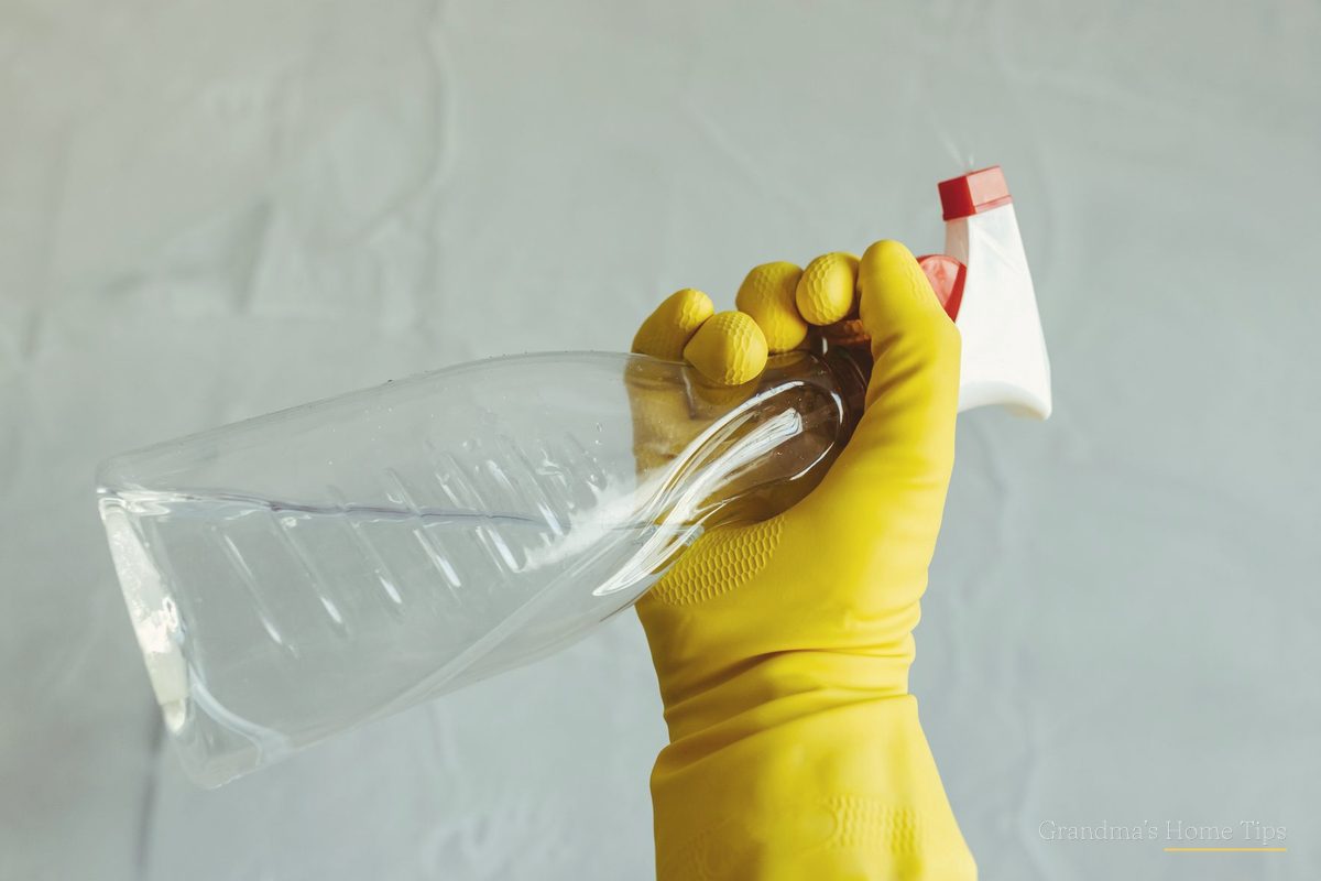 Hand in a yellow rubber glove holding a spray bottle of vinegar cleaning solution